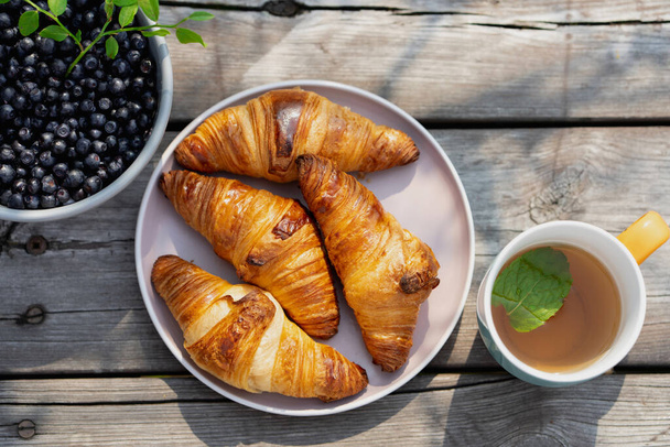 Minttutee, mustikka croissantit ja mustikat puupöydällä kesäpuutarhassa - Valokuva, kuva