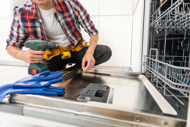 Service man repareert vaatwasser in moderne keuken. Onderhoud en huishoudelijke hulp concept. Hoge kwaliteit foto - Foto, afbeelding