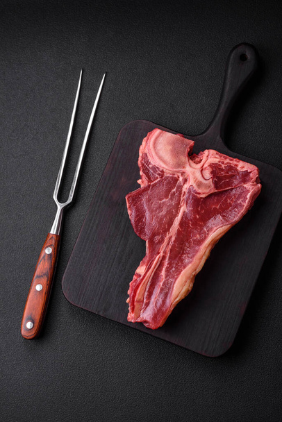 Syrový čerstvý šťavnatý hovězí steak se solí, kořením a bylinkami na tmavém betonovém pozadí - Fotografie, Obrázek