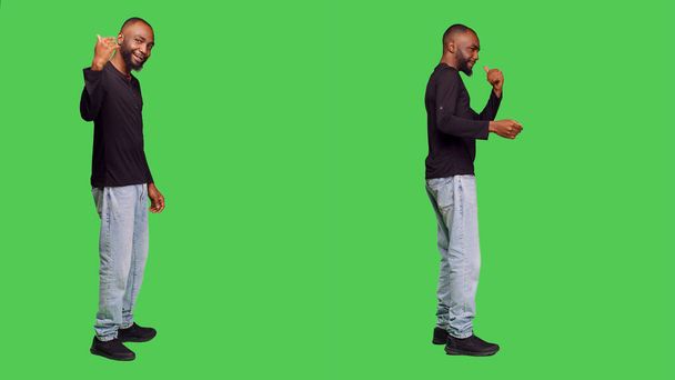 Afrykański Amerykanin prosi kogoś, by przyszedł, pozował w dżinsach i koszuli na zielonym ekranie. mężczyzna model stojąc w studio i wzywając ktoś dla towarzyszyć lub dołączyć. - Zdjęcie, obraz