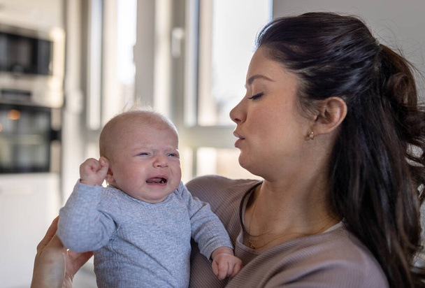 Preocupada madre sosteniendo al bebé llorando en casa - Foto, imagen