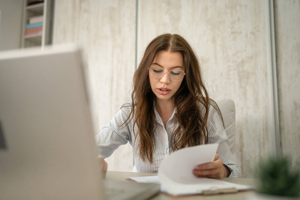Beyaz kadın girişimci işkadını ya da sekreter masasında oturmuş kağıt belgelerini kontrol ediyor tişört fotokopi odası giyiyor. - Fotoğraf, Görsel