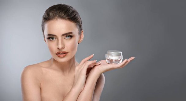 Beautiful woman with perfect skin holding a jar of lotion or creme isolated on a grey background with copy space. Cosmetics, dermatology, antiaging concept. Banner for advertising a skincare product. - Photo, Image