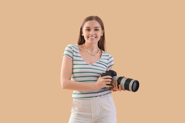 Joven fotógrafa con cámara profesional sobre fondo beige - Foto, imagen