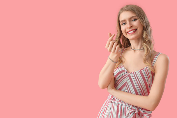 Fiatal nő, hogy szív az ujjaival rózsaszín háttér - Fotó, kép