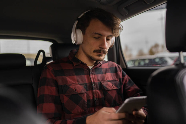 een man volwassen blanke man zitten in de auto met koptelefoon op zijn hoofd luisteren naar de muziek of podcast, terwijl het nemen van een rem tijdens het reizen wachten en ontspannen echte mensen kopiëren ruimte moderne levensstijl - Foto, afbeelding