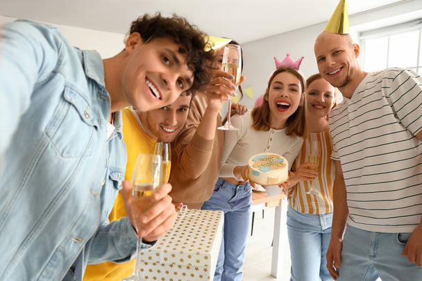 Grupa młodych przyjaciół z tortem urodzinowym robi selfie w kuchni - Zdjęcie, obraz
