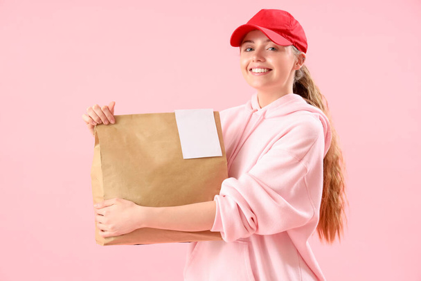Γυναικείος κούριερ με χάρτινη τσάντα σε ροζ φόντο - Φωτογραφία, εικόνα