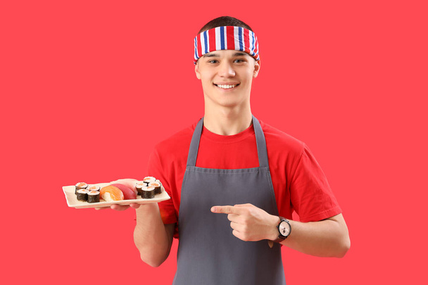 Молодий чоловік в фартусі і зі смачними суші на червоному тлі - Фото, зображення