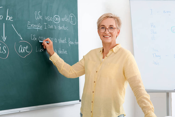 Female teacher writing English grammar on chalkboard in classroom - Photo, Image