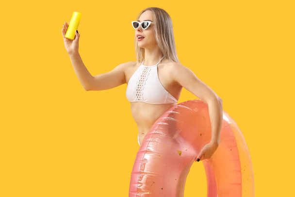 Young woman with sunscreen cream and inflatable ring on yellow background - Photo, Image