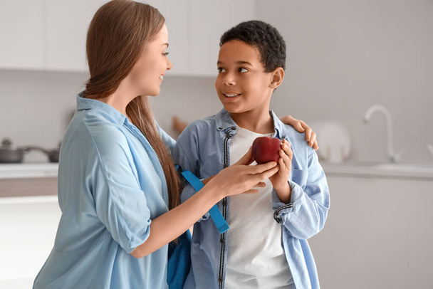 Mother giving apple to little schoolboy in kitchen - Photo, Image
