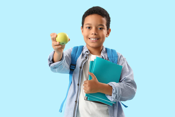 Mały afro-amerykański uczeń z książkami i jabłkiem na jasnoniebieskim tle - Zdjęcie, obraz
