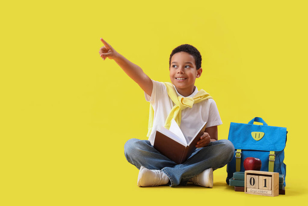 Kleine Afro-Amerikaanse schooljongen met boek, rugzak, kalender en appel op gele achtergrond - Foto, afbeelding