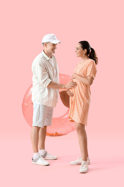 Young pregnant couple with inflatable ring on pink background - Photo, Image
