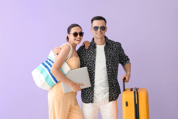 Junges Paar mit Taschen und Laptop auf fliederfarbenem Hintergrund - Foto, Bild
