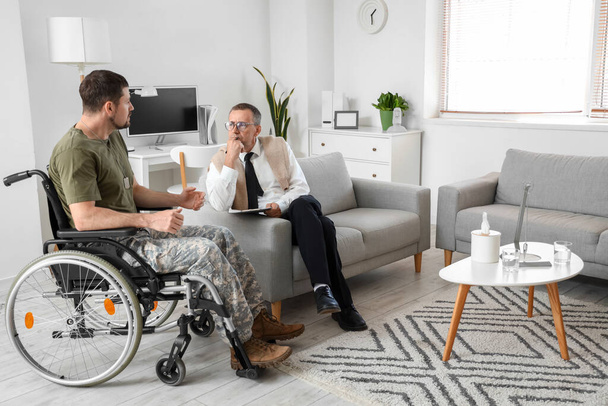 Volwassen psycholoog werkt met soldaat in rolstoel op kantoor - Foto, afbeelding
