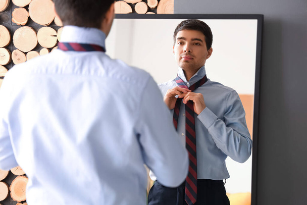 Jeune homme d'affaires attacher sa cravate devant le miroir à la maison - Photo, image
