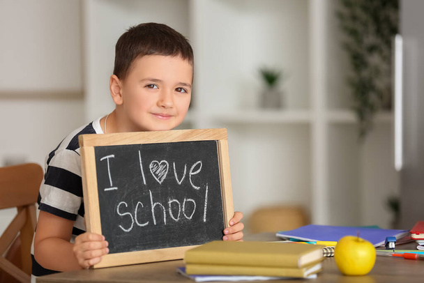 Lindo niño sosteniendo pizarra con texto I LOVE SCHOOL en casa - Foto, imagen