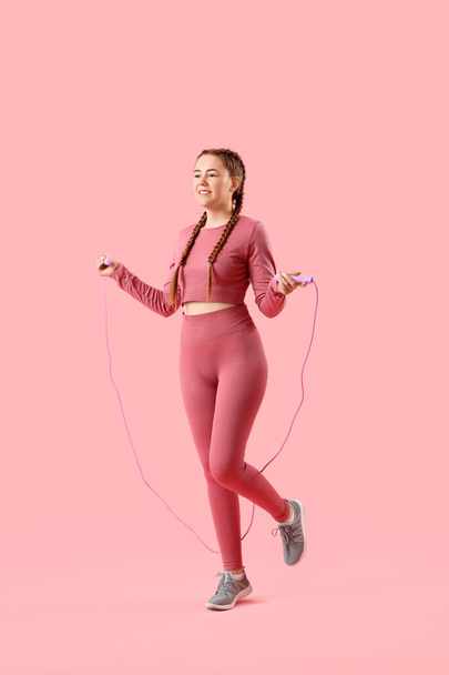 Sportliche junge Frau springt mit Seil auf rosa Hintergrund - Foto, Bild
