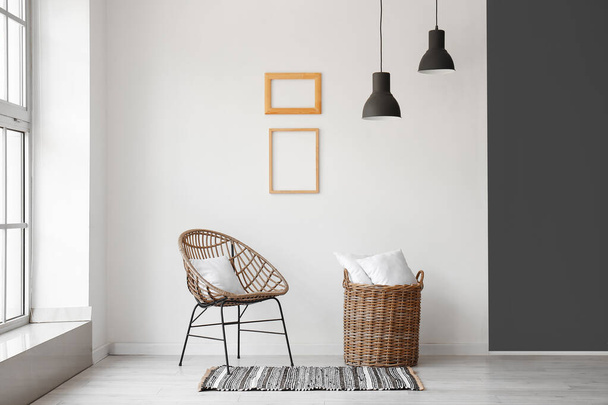 Плетеное кресло и корзина с подушками возле белой стены - Фото, изображение