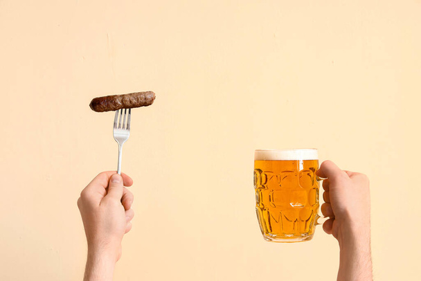 Человек со стаканом пива и колбасой на бежевом фоне - Фото, изображение