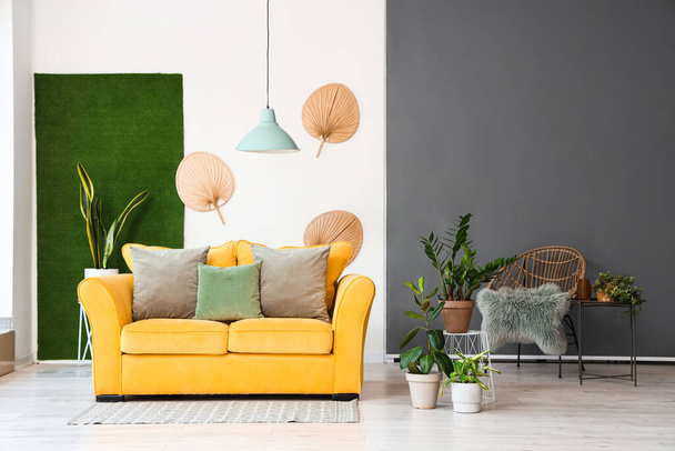 Интерьер светлой гостиной с желтым диваном и комнатными растениями - Фото, изображение