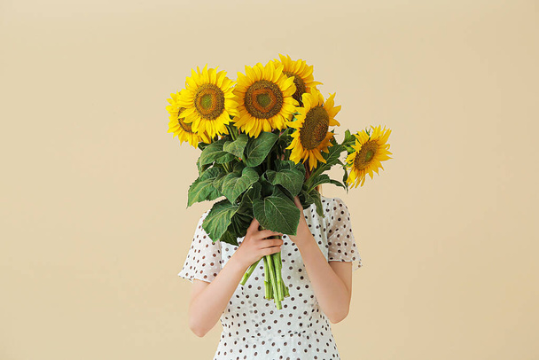 Frau mit schönen Sonnenblumen auf beigem Hintergrund - Foto, Bild