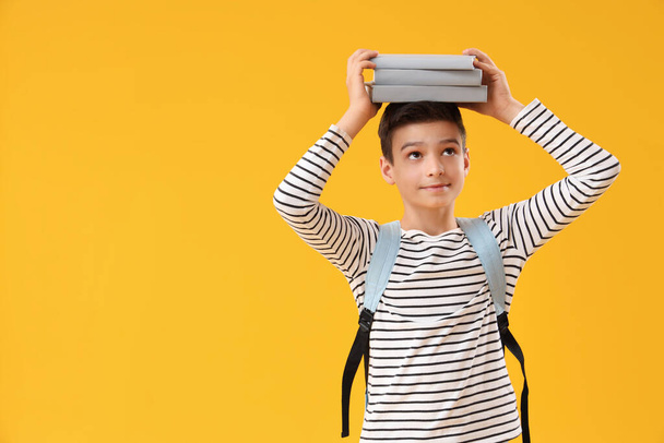 Portré iskolás fiú hátizsák gazdaság könyvek a fején, narancssárga háttér - Fotó, kép