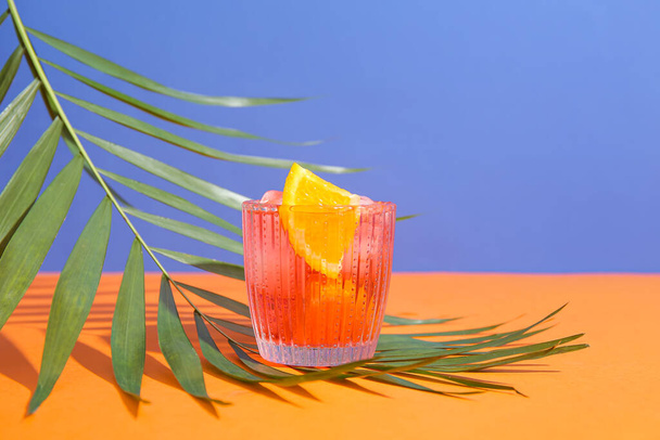 Szklanka zimnego Negroni koktajl i liść palmowy na tle koloru - Zdjęcie, obraz