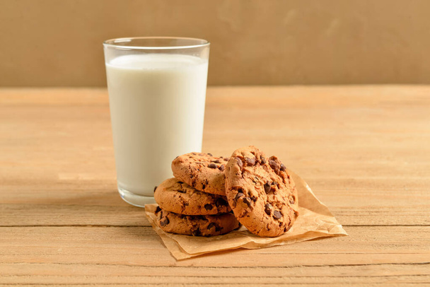 Çikolata parçacıklı kurabiyeler ve masada bir bardak süt. - Fotoğraf, Görsel