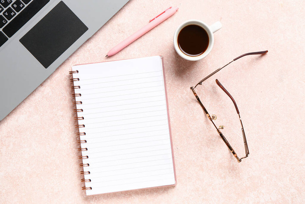 Notitieboek met laptop en kopje smakelijke koffie op roze achtergrond - Foto, afbeelding
