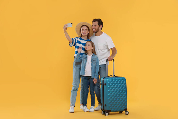 Happy family with suitcase taking selfie on orange background - Photo, Image