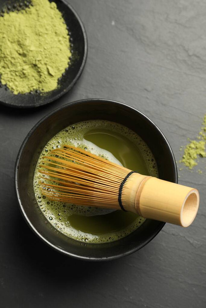 Cup of fresh matcha tea with bamboo whisk on black table, flat lay - Foto, Imagem