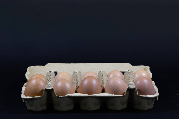 Scatto in studio di una scatola isolata di uova su fondo nero contenente uova marroni, ra e biologiche, pronte per essere cotte. - Foto, immagini