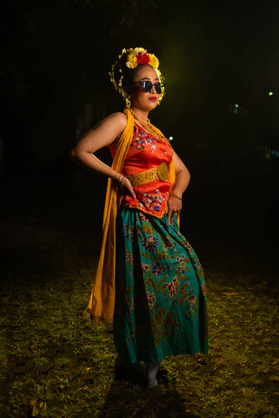 eine traditionelle javanische Tänzerin steht und tanzt mit einem flexiblen Körper und trägt nachts eine Sonnenbrille - Foto, Bild