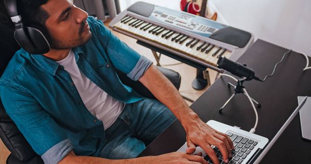 Ασιάτης μουσικός δημιουργεί νέα μουσική στο στούντιο του σπιτιού του. Ένας συνθέτης χρησιμοποιεί σύγχρονο εξοπλισμό για να δημιουργήσει μια μελωδία.. - Φωτογραφία, εικόνα