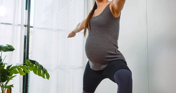 Azji w ciąży kobieta w odzieży sportowej robi ćwiczenia w salonie w domu. - Zdjęcie, obraz
