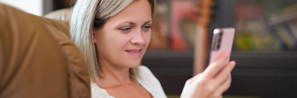 Kobieta uśmiechnięta czytając wiadomości na komórce. Szczęśliwa kobieta patrząc na ekran smartfona w domu. - Zdjęcie, obraz