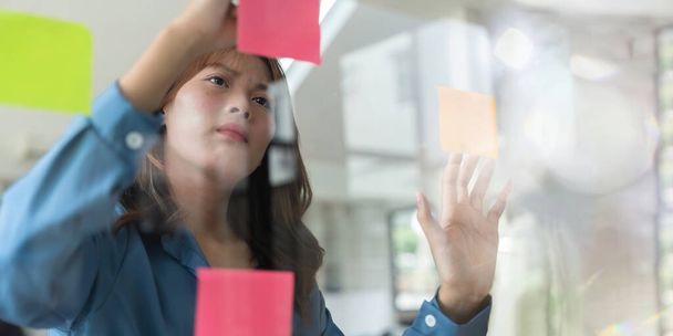 Joven mujer asiática frente al espejo mientras recoge lluvia de ideas en la oficina y la estrategia de trabajo. - Foto, Imagen