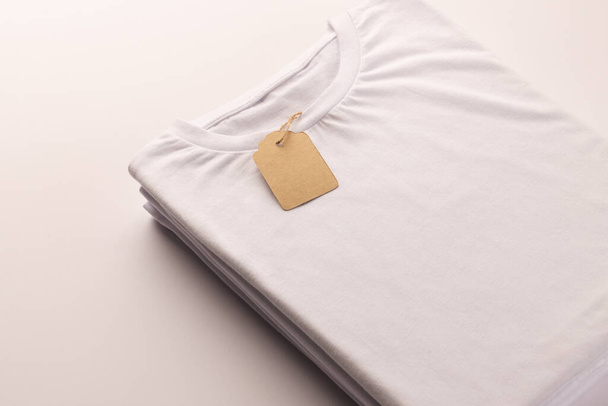 Stack of white t shirts with tag and copy space on white background. Fashion, clothes, colour and fabric concept. - Fotó, kép