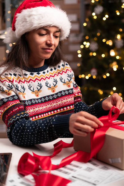 Mujer con sombrero de Santa Claus trabaja en un almacén de cajas con regalos de embalaje regalos para la tienda en línea para la Navidad. El dueño de una pequeña empresa vende feliz año nuevo. Vacaciones de entrega. Copiar espacio - Foto, imagen