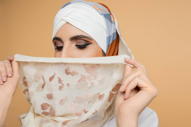 modesta donna musulmana con trucco viso oscuro con elegante velo di seta su beige - Foto, immagini