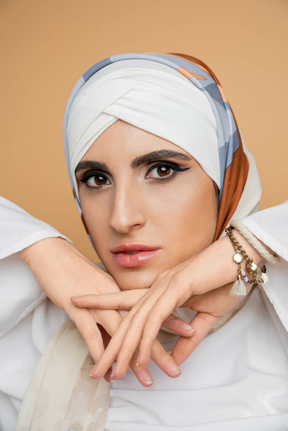 Çekici Müslüman kadın portresi. Makyajlı, ipek eşarplı, elleri bej üzerine yakın. - Fotoğraf, Görsel