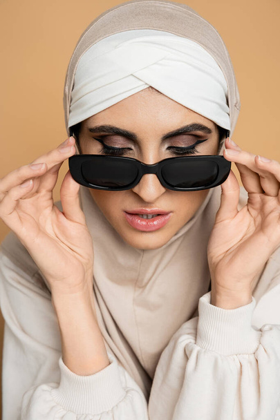 encantadora mujer musulmana en hijab quitándose las gafas de sol de moda en color beige, estilo personal, individualidad - Foto, Imagen