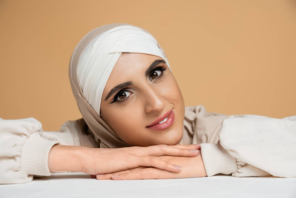 ritratto di donna mediorientale in hijab, con trucco guardando la macchina fotografica su beige, bellezza musulmana - Foto, immagini