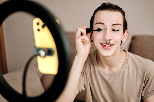 Homosexuell Mann Anwendung Wimpern während der Aufnahme eines Online-Videos mit dem Handy zu Hause - Foto, Bild