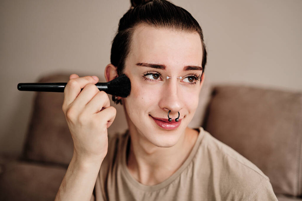 close-up portret van een schattig gay man met behulp van make-up borstel thuis - Foto, afbeelding