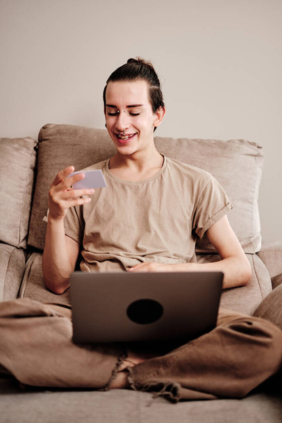 Vertical retrato de um gay compras on-line sentado no sofá em casa - Foto, Imagem
