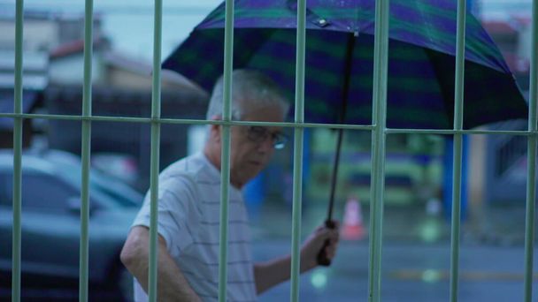 Älterer älterer Mann bereitet sich bei regnerischem Abend auf Spaziergang vor und öffnet Regenschirm auf Straßenseite - Foto, Bild